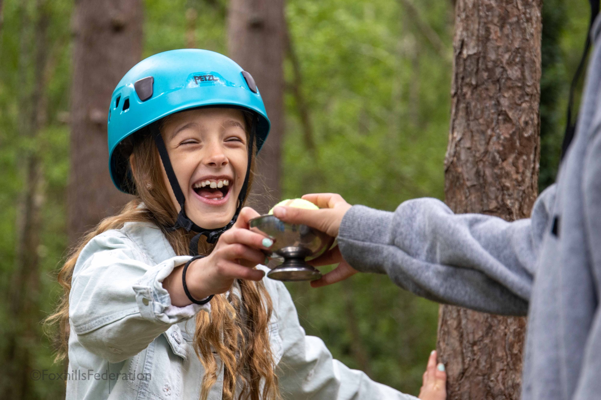 A girl laughs while passing a ball in a egg cup