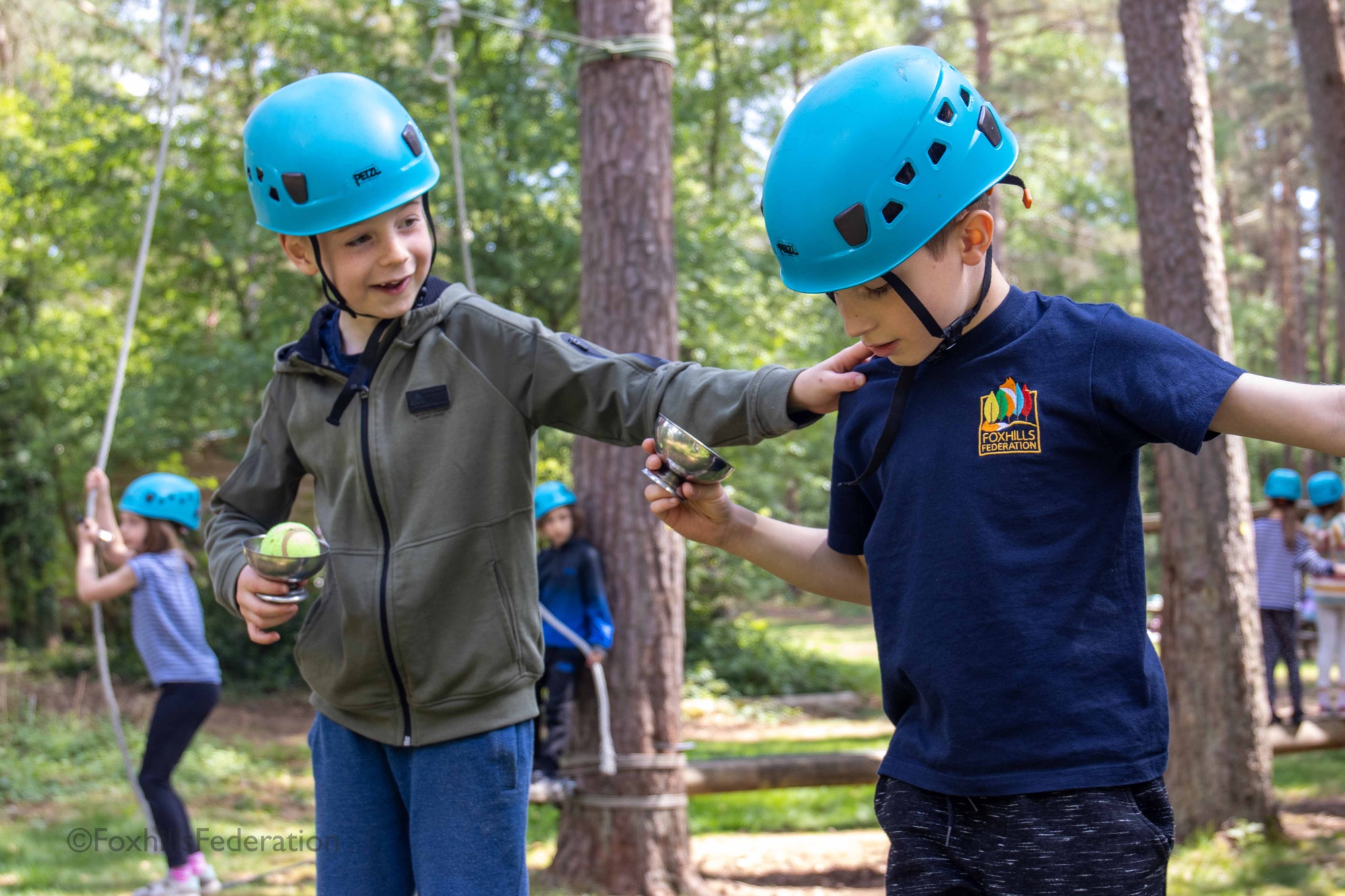 Two boys help each other across a rope course