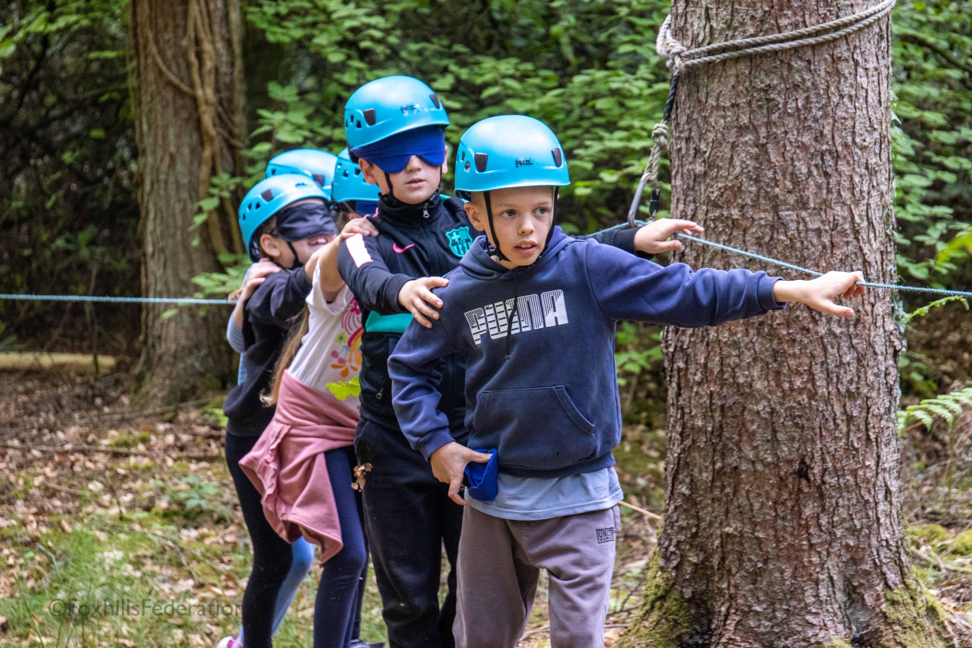 A boy leads a group of blindfolded children through a trail