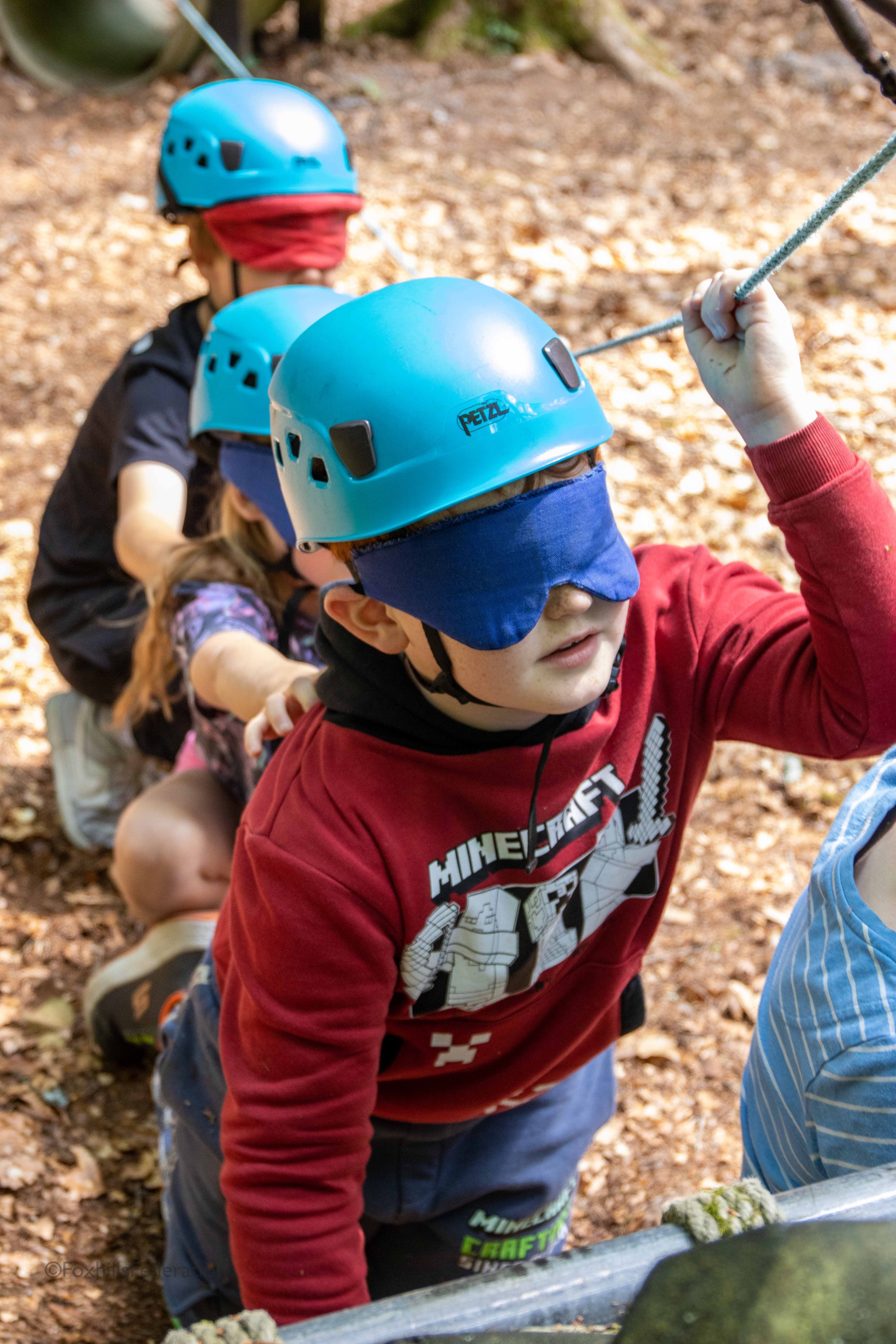 A blindfolded boy leads a group of children through a trail
