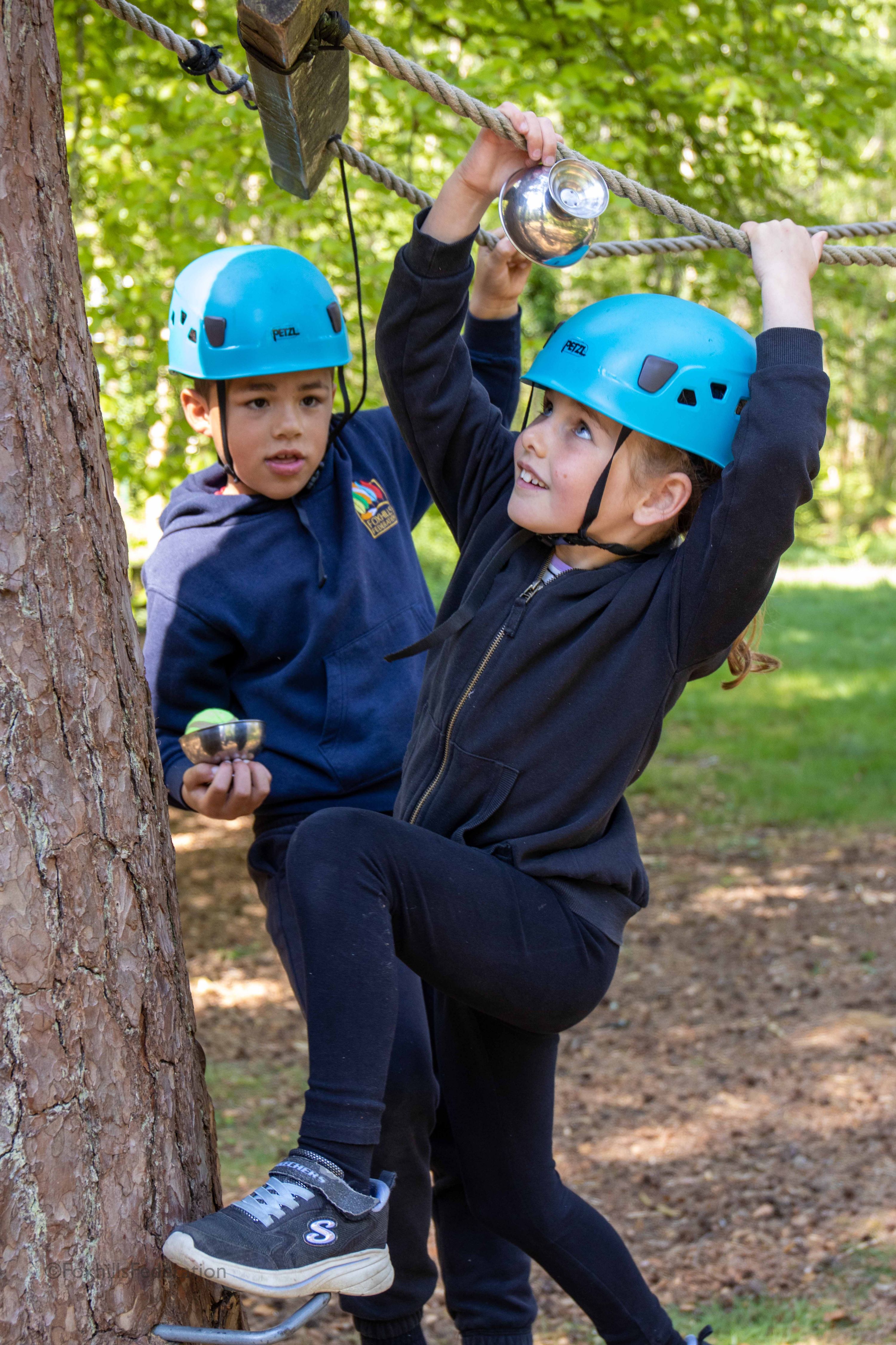 Two children help each other across a rope course