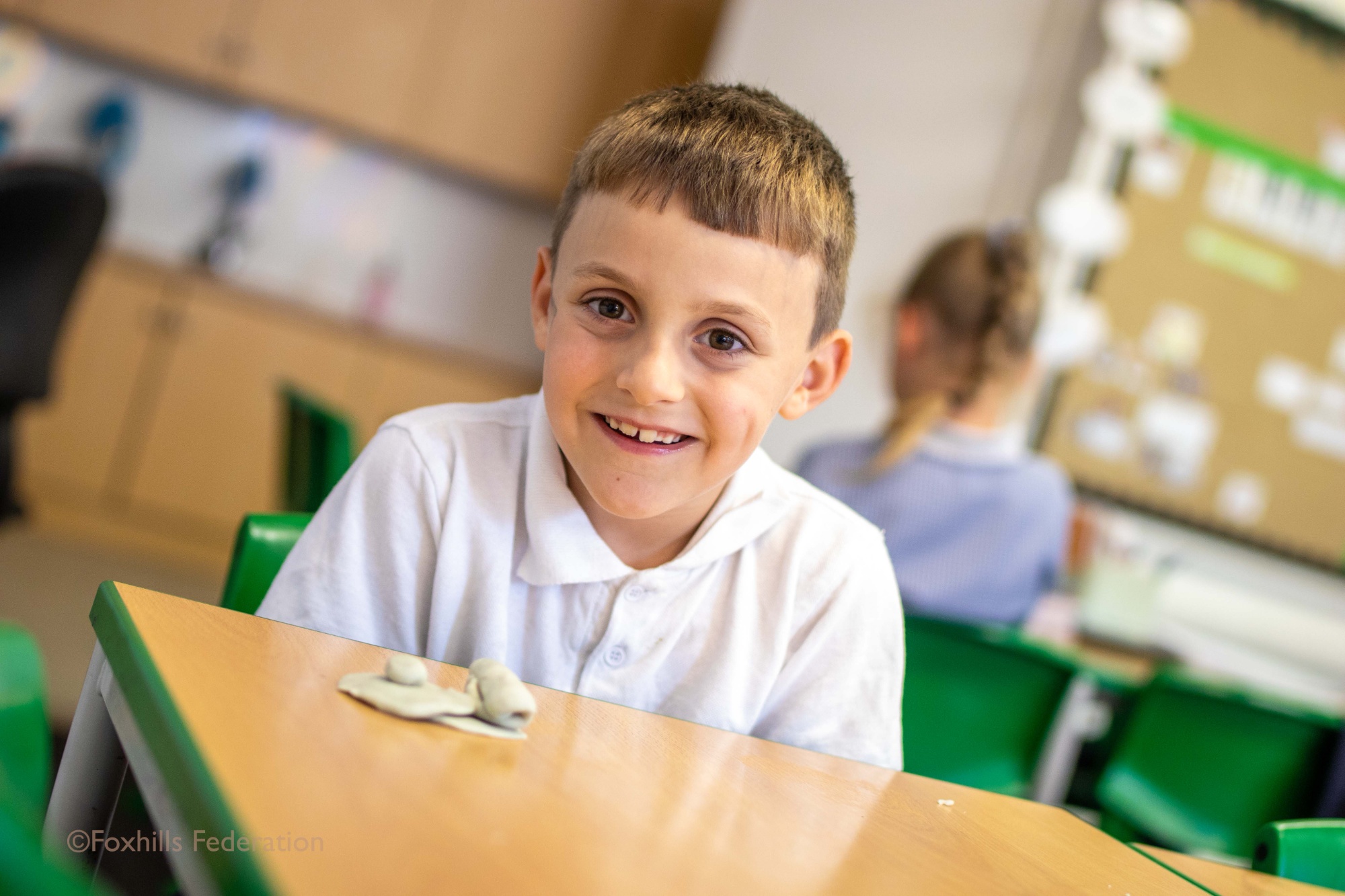A Foxhills pupil smiling at the camera with a plasticine creation in front of him.