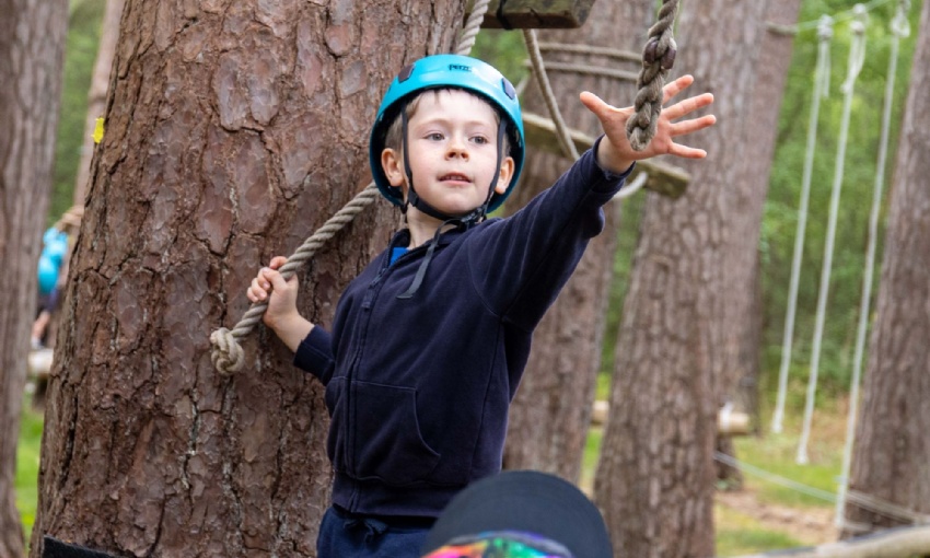 A boy grabs at a rope on a low rope course